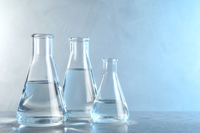 Photo of Laboratory glassware with liquid samples for analysis on table against toned blue background, space for text