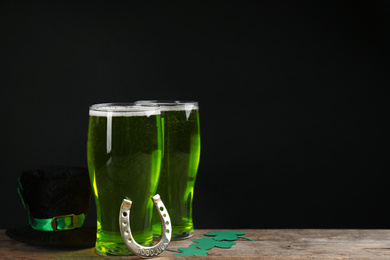 Composition with green beer and clover leaves on wooden table against black background, space for text. St. Patrick's Day celebration