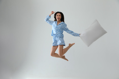 Photo of Beautiful Asian woman with pillow jumping on light grey background. Bedtime