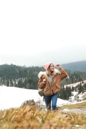 Young woman in warm clothes near snowy hill. Winter vacation