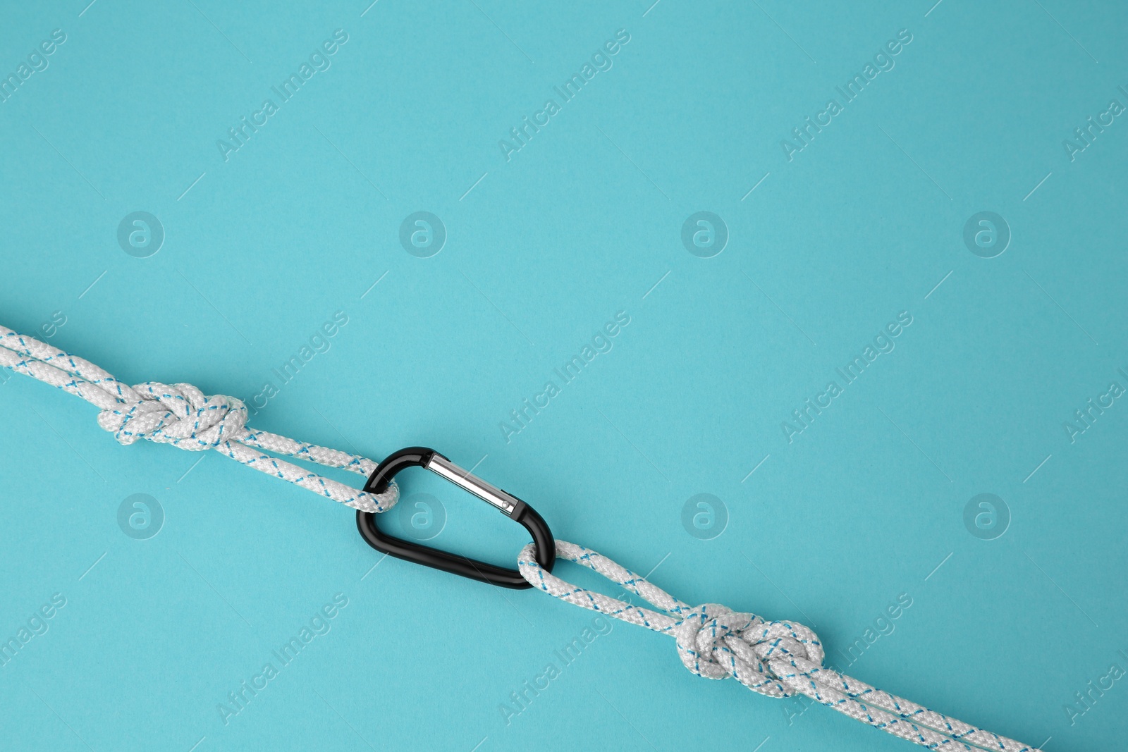 Photo of One metal carabiner with ropes on light blue background, top view. Space for text