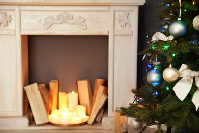 Photo of Decorative fireplace with wood near Christmas tree indoors. Stylish room interior