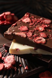 Photo of Board and different chocolate bars with freeze dried fruits on wooden table, closeup