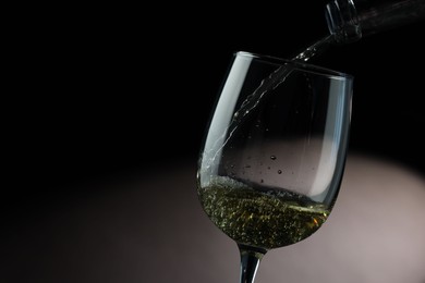 Photo of Pouring tasty aromatic wine in glass on dark background, closeup. Space for text