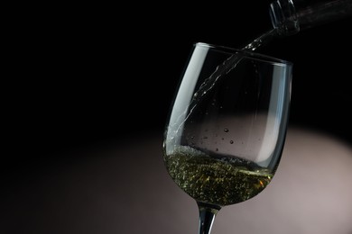 Pouring tasty aromatic wine in glass on dark background, closeup. Space for text