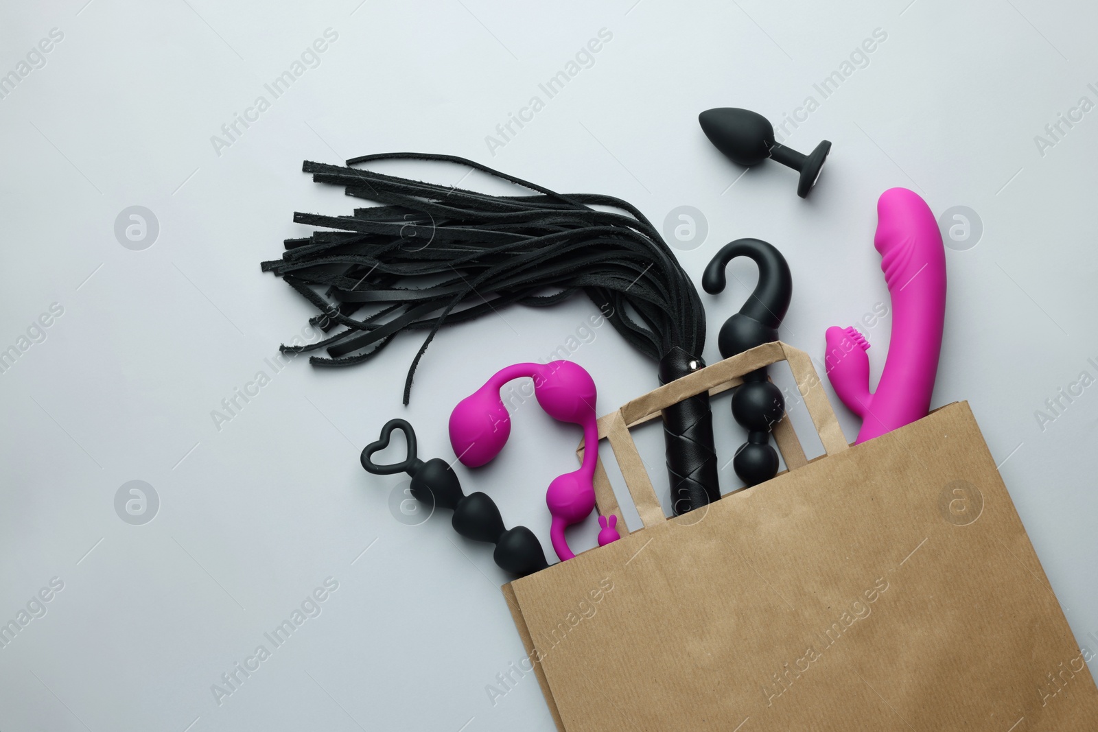 Photo of Paper shopping bag with different sex toys on white background, flat lay