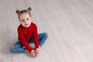 Photo of Cute little girl sitting on warm floor indoors, space for text. Heating system