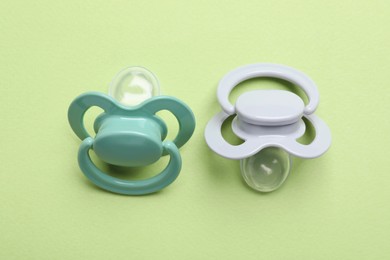 Two baby pacifiers on pale green background