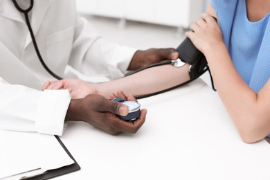 Photo of Young African-American doctor checking patient's pulse and blood pressure in hospital