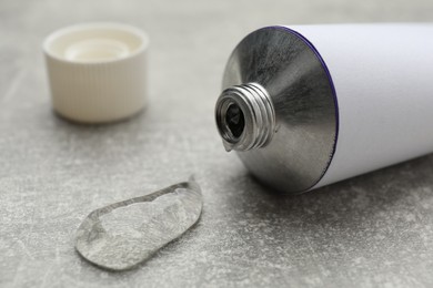 Photo of Open white tube with ointment on light grey table, closeup