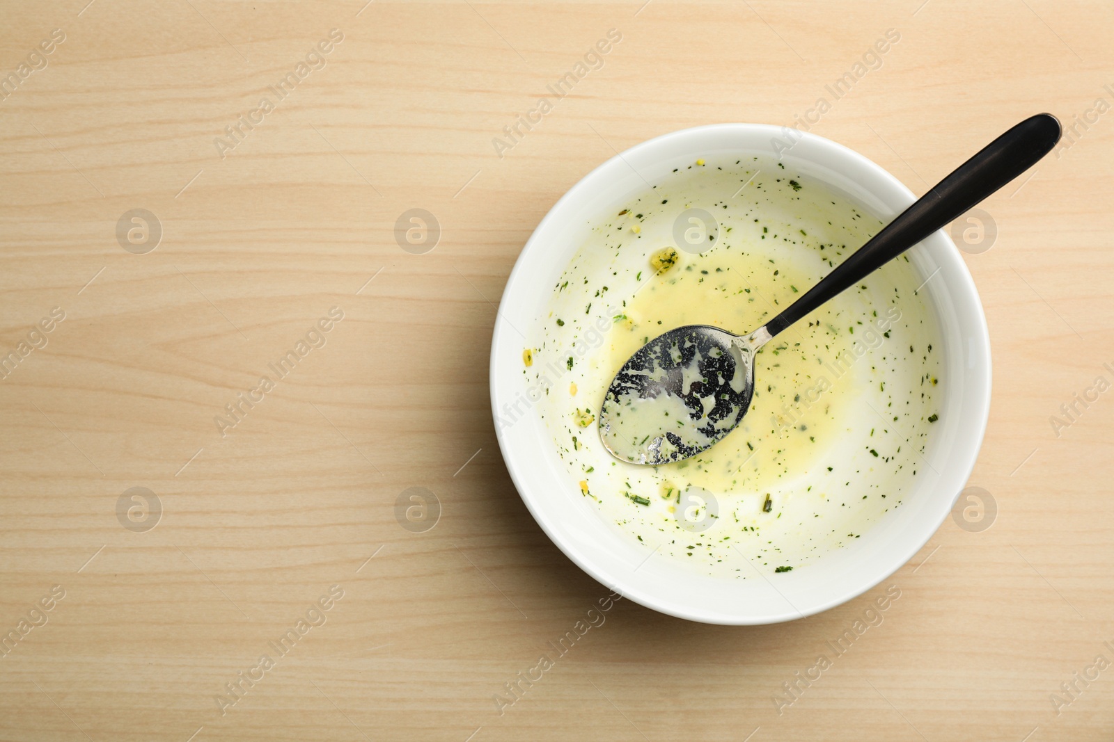 Photo of Dirty bowl with food leftovers and spoon on wooden background, top view. Space for text