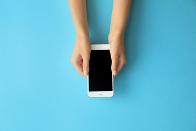 Photo of Woman holding modern phone on blue background, top view. Space for text