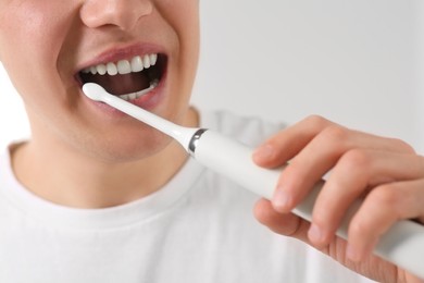 Man brushing his teeth with electric toothbrush on blurred background, closeup
