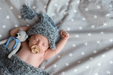 Photo of Cute newborn baby in warm hat with toy sleeping on bed, top view. Space for text