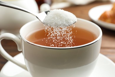 Photo of Adding sugar into cup of tea at table, closeup
