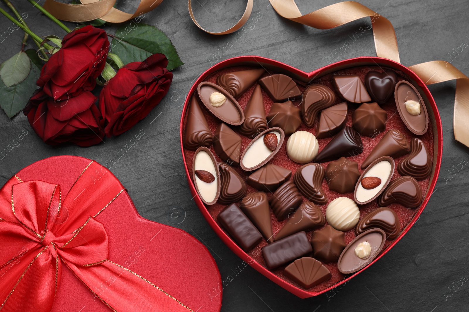 Photo of Heart shaped box with delicious chocolate candies, roses and ribbon on grey table, flat lay