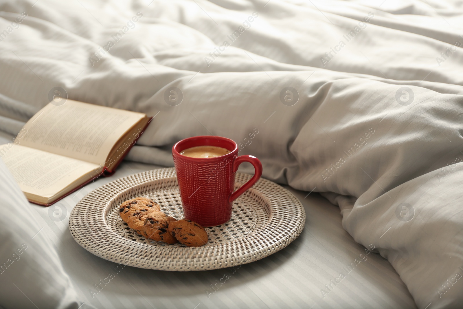 Photo of Cup of aromatic coffee, cookies and book on bed with soft blanket