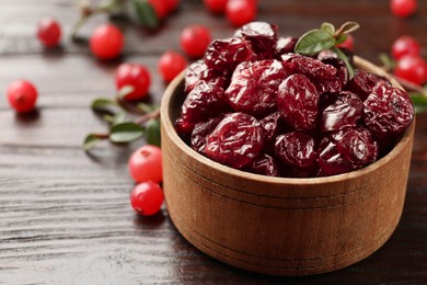 Photo of Tasty dried cranberries in bowl, fresh ones and leaves on wooden table, closeup. Space for text