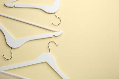 Photo of White hangers on pale yellow background, flat lay. Space for text