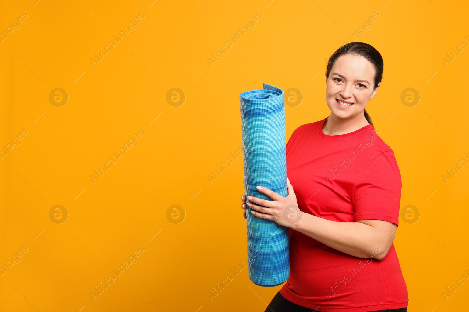 Photo of Happy overweight woman with yoga mat on orange background, space for text