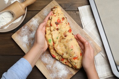 Photo of Woman making Stollen with candied fruits and raisins on wooden board at table, top view