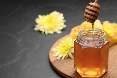 Photo of Pouring sweet honey from dipper into jar at grey table, space for text