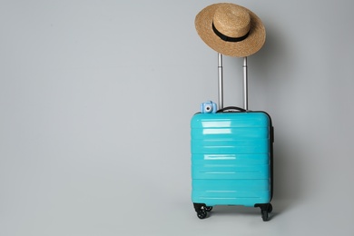 Photo of Travel suitcase with hat and camera on light grey background, space for text. Summer vacation