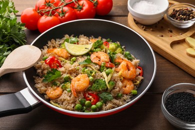 Photo of Tasty rice with shrimps and vegetables in frying pan on wooden table, closeup