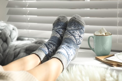 Photo of Woman with cocoa wearing knitted socks at home, closeup. Warm clothes
