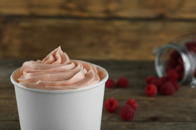 Photo of Cup with tasty frozen yogurt and raspberries on wooden table, closeup. Space for text