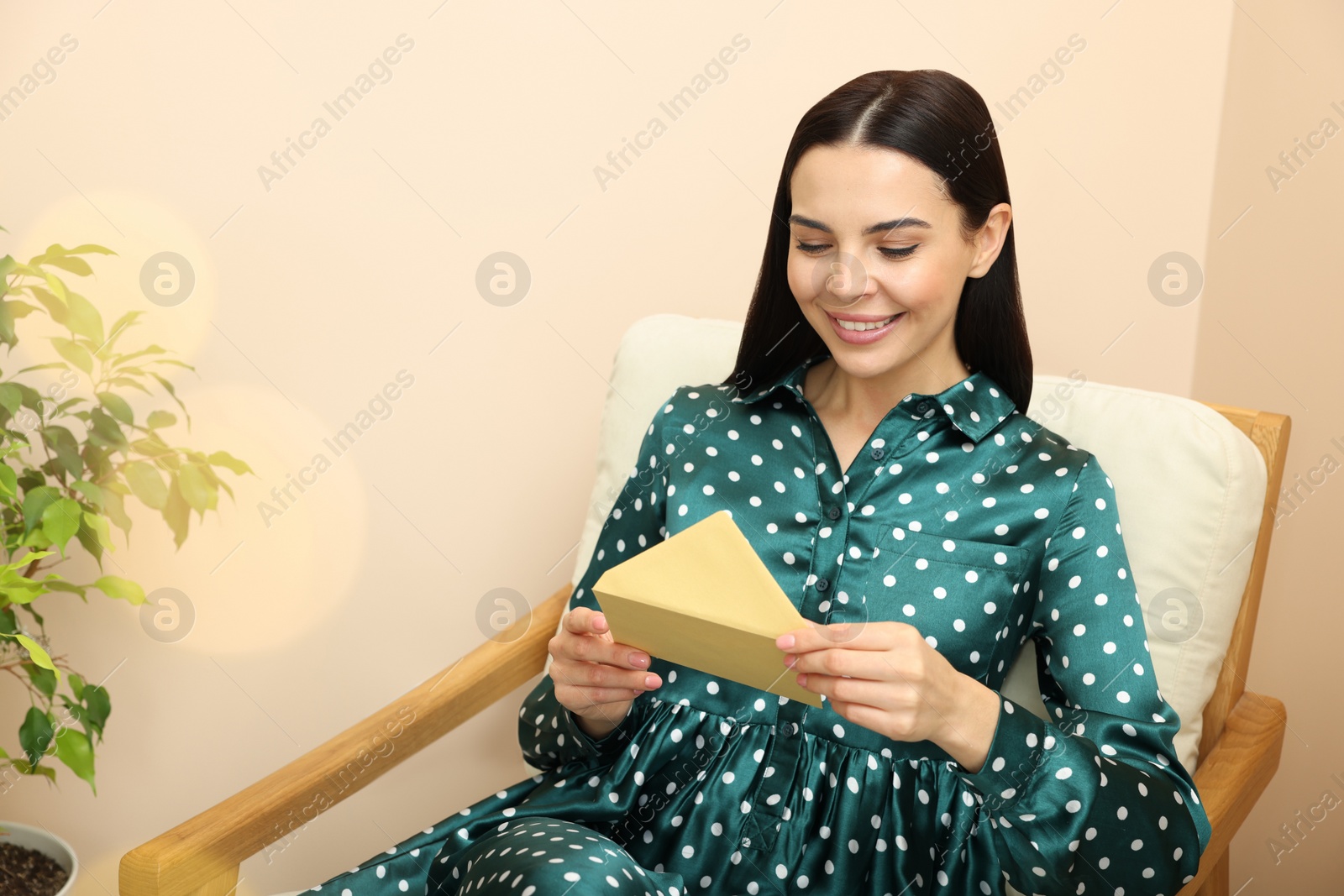 Photo of Happy woman reading greeting card on armchair in living room