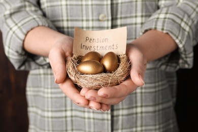 Photo of Woman holding golden eggs and card with phrase Pension Investments in nest, closeup