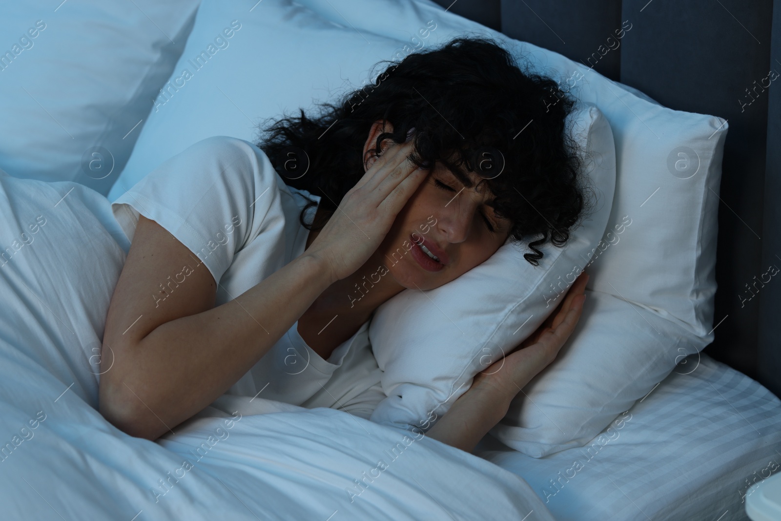 Photo of Young woman suffering from headache in bed at night