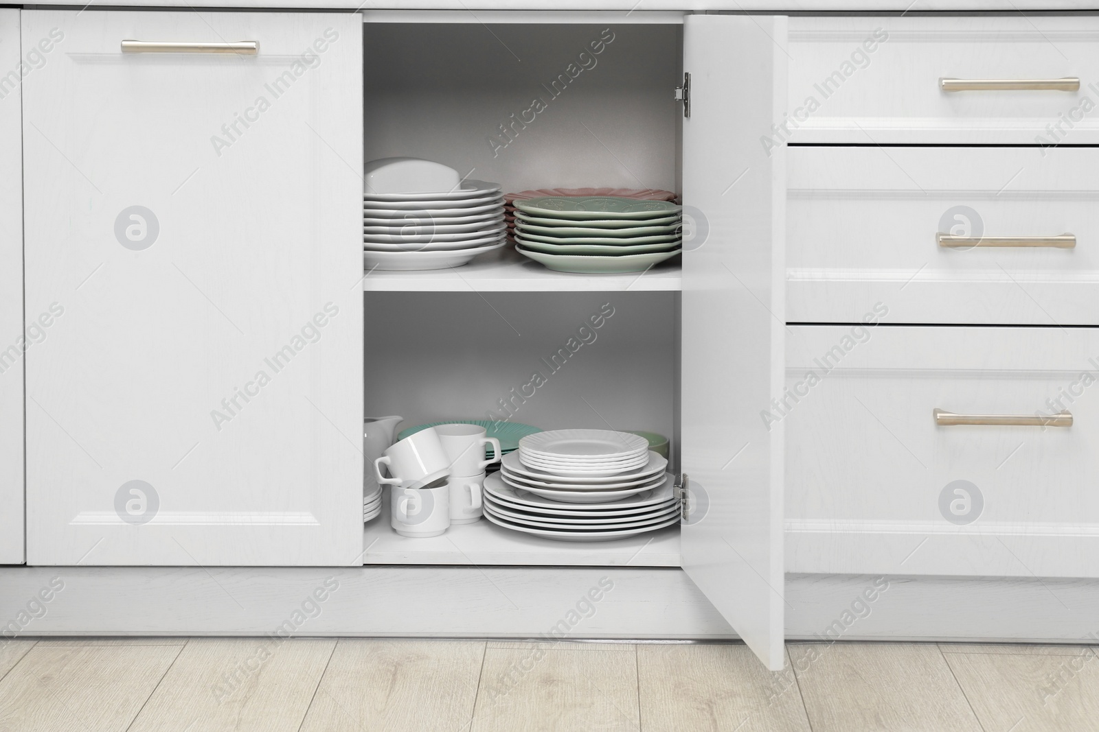 Photo of Clean plates and other crockery on shelves in cabinet indoors