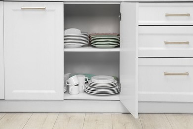 Clean plates and other crockery on shelves in cabinet indoors