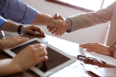 Photo of Business partners shaking hands at table after meeting in office, closeup