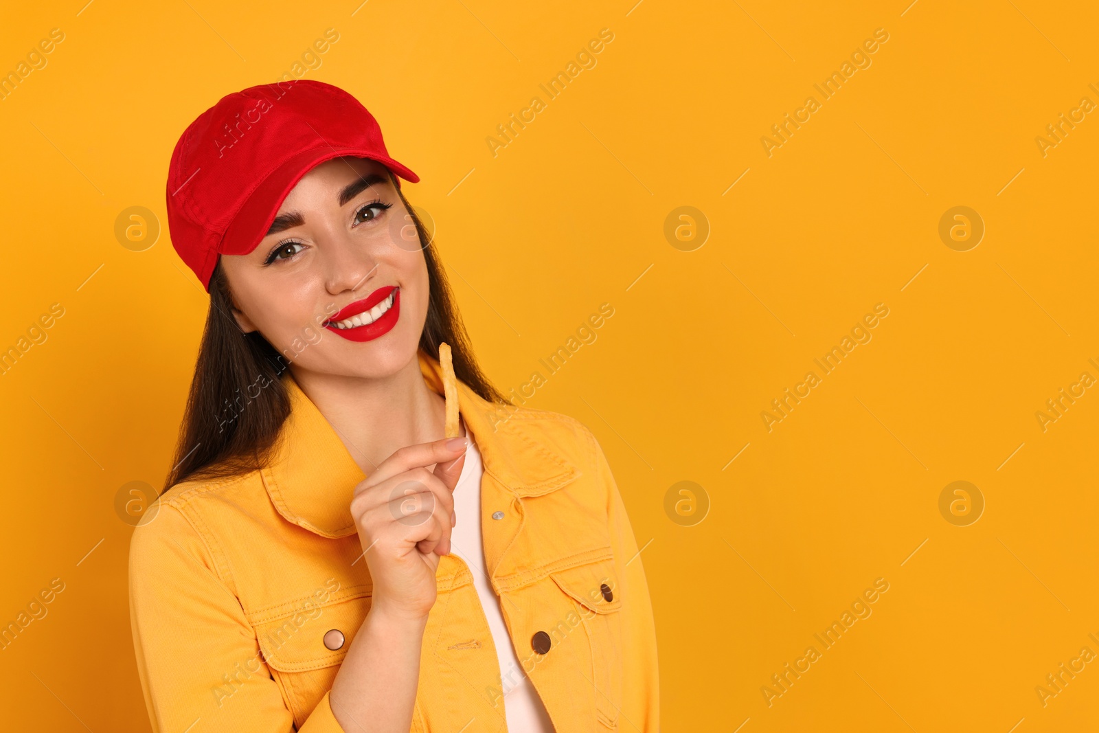 Photo of Beautiful young woman eating French fries on yellow background. Space for text