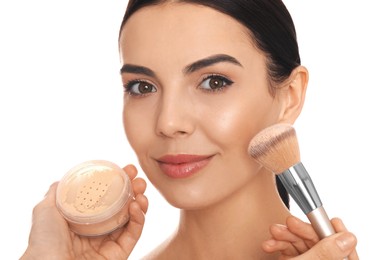 Professional makeup artist applying powder onto beautiful young woman's face with brush on white background, closeup