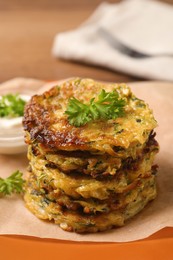 Delicious zucchini pancakes and bowl with sour cream on table, closeup