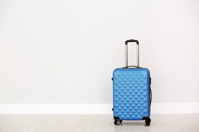 Modern suitcase on floor near light wall. Space for text