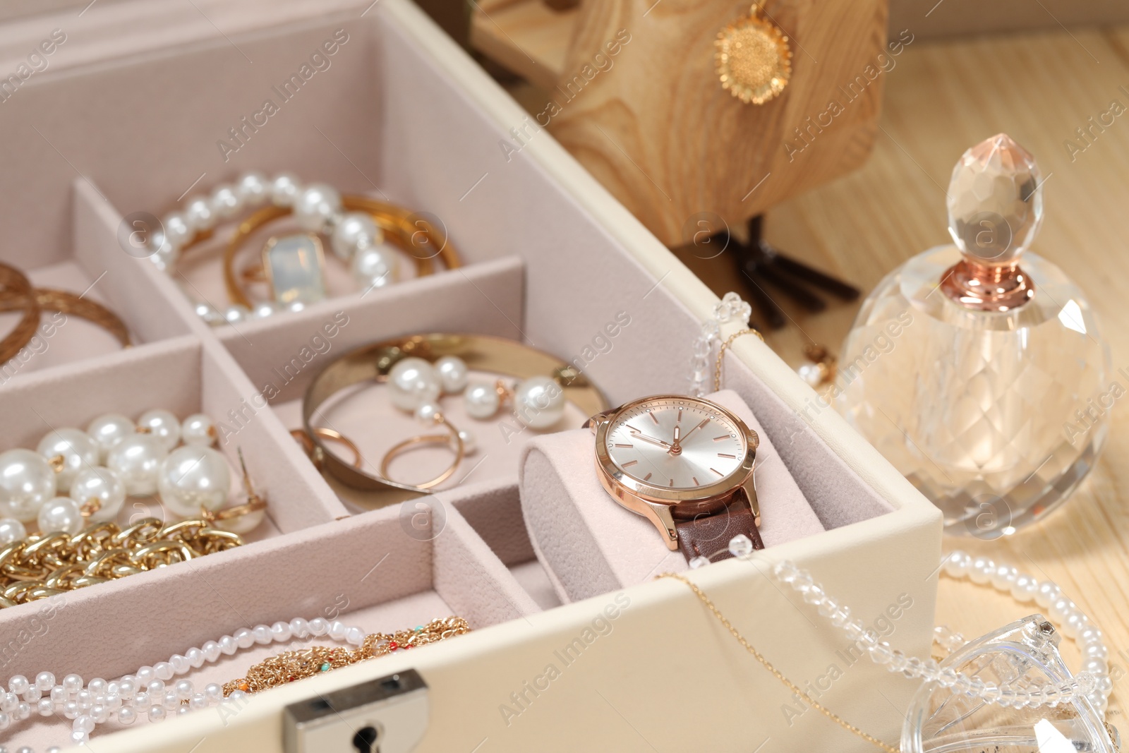 Photo of Jewelry box with many different accessories and perfume on wooden table, closeup