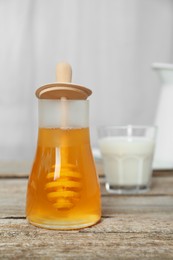 Photo of Jar with honey and glass of milk on wooden table