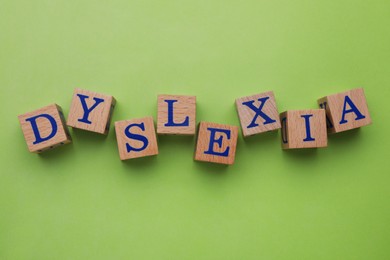 Wooden cubes with word Dyslexia on light green background, flat lay