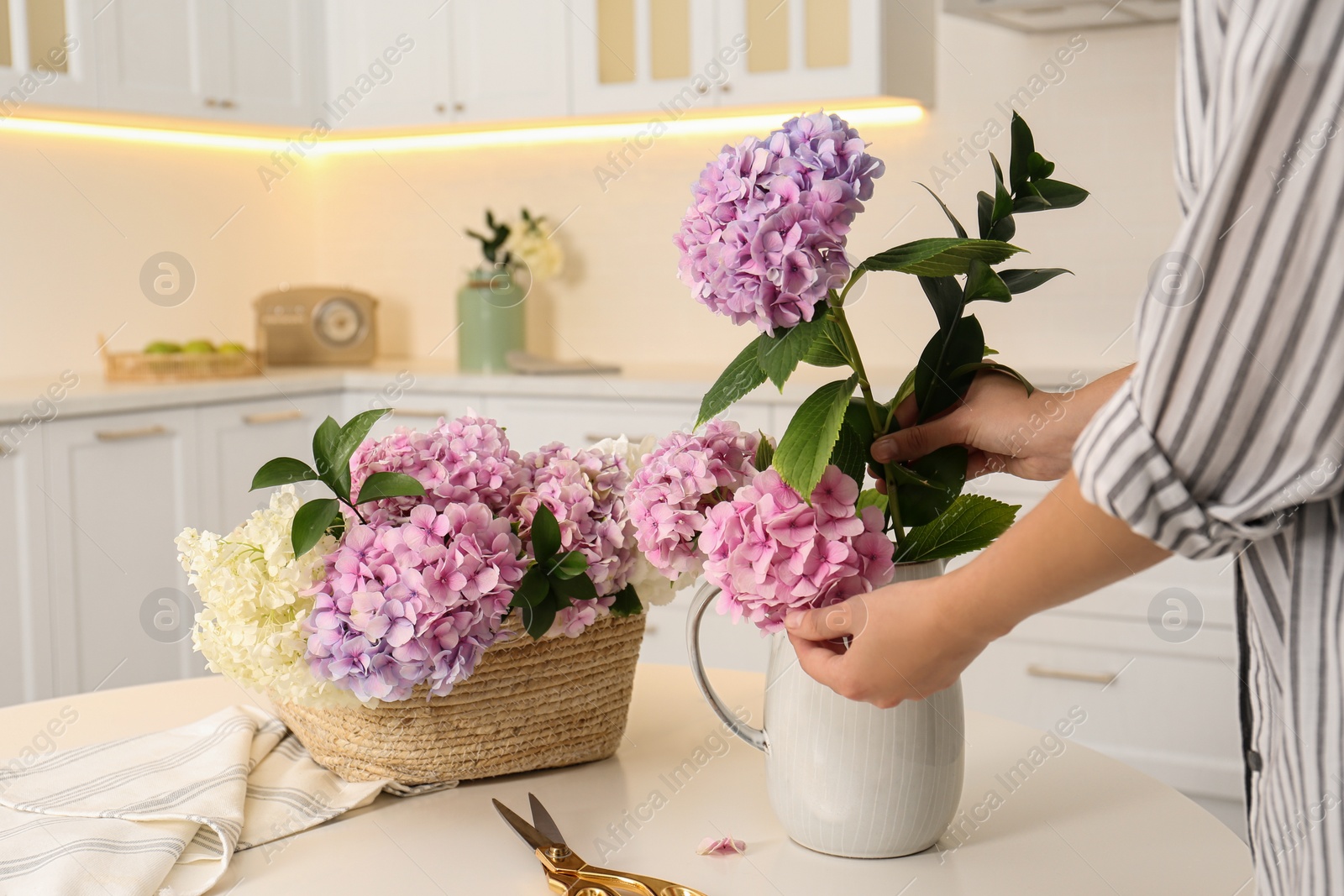 Photo of Woman making bouquet with beautiful hydrangea flowers at table indoors, closeup. Interior design element