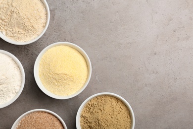 Bowls with different types of flour on grey background, top view. Space for text