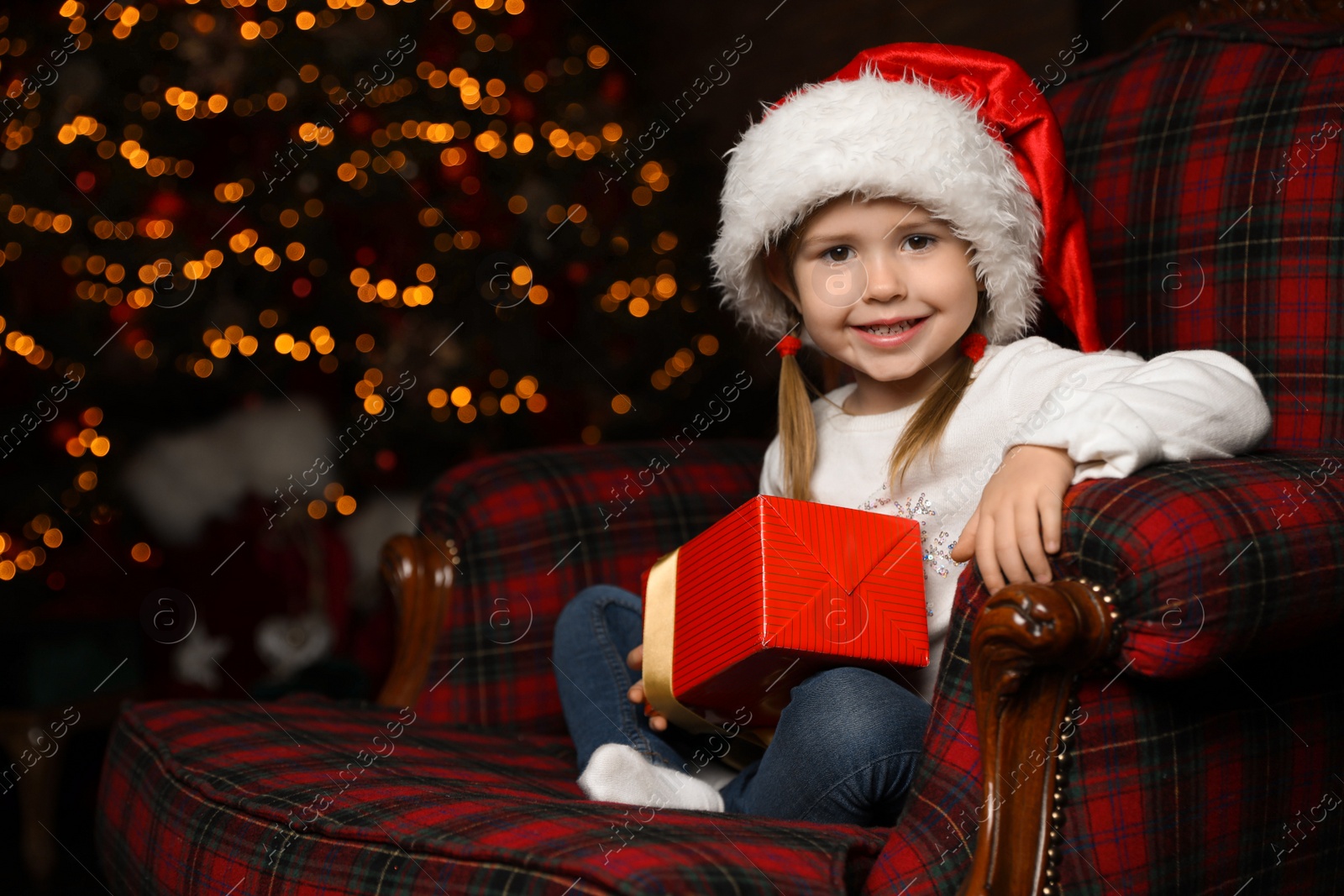 Photo of Cute little child with Christmas gift sitting in armchair at home