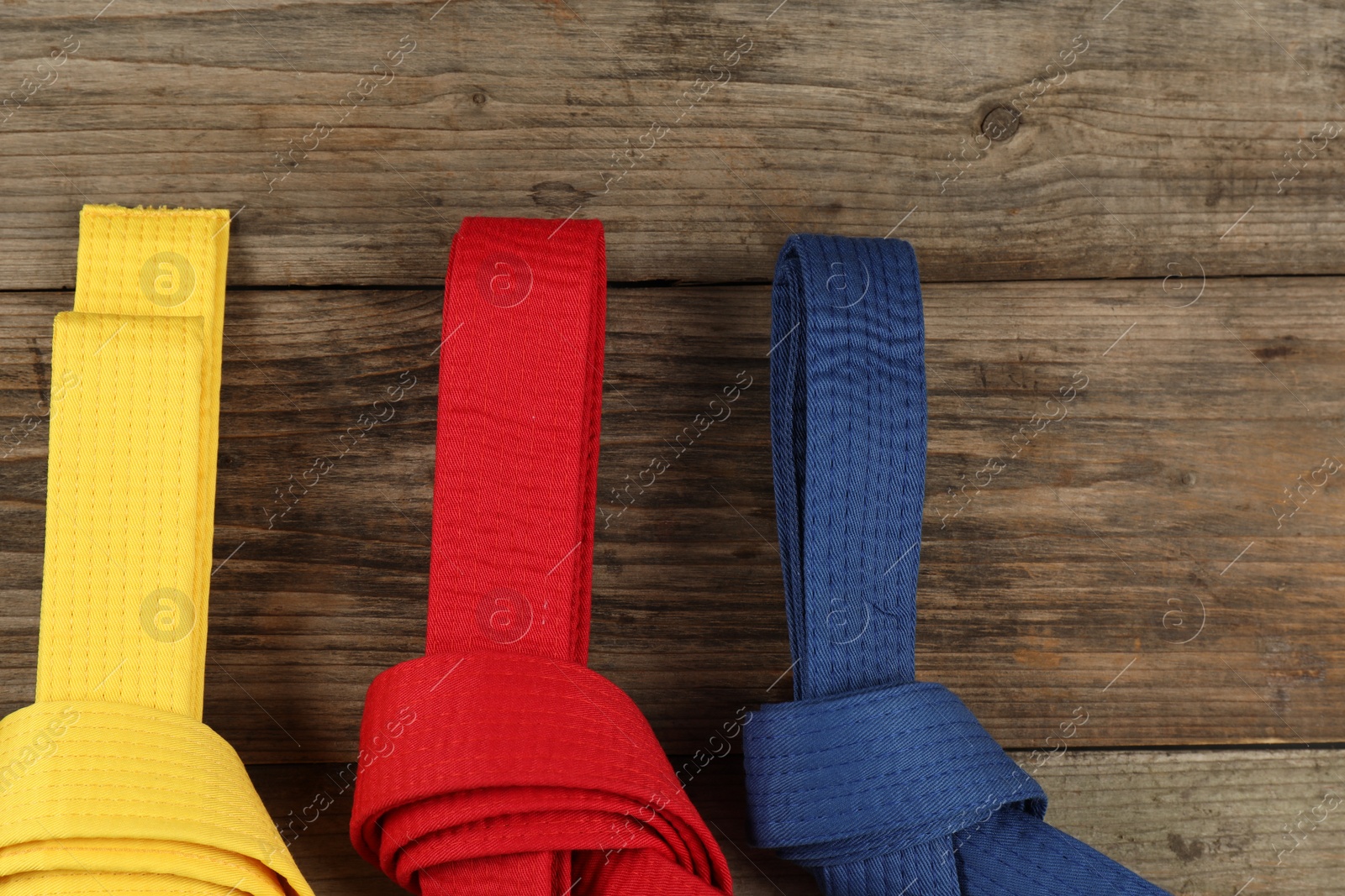 Photo of Colorful karate belts on wooden background, flat lay