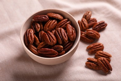 Photo of Tasty pecan nuts with bowl on beige cloth, closeup