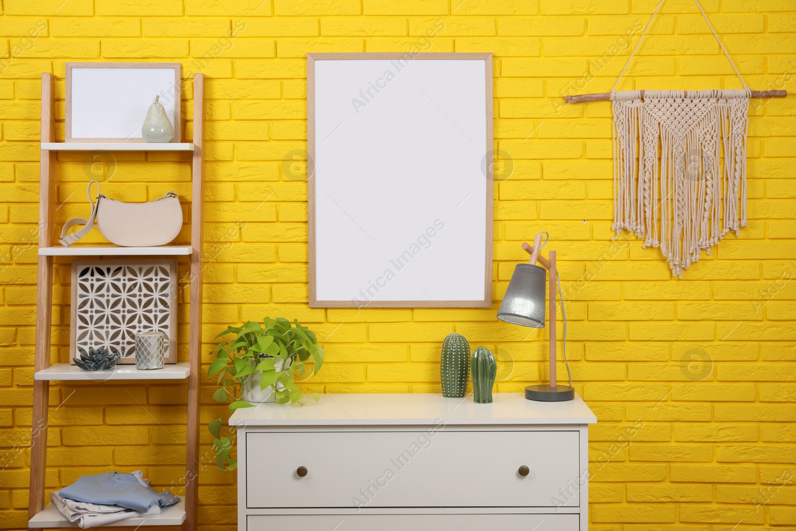 Photo of Empty frame hanging on yellow brick wall indoors. Mockup for design