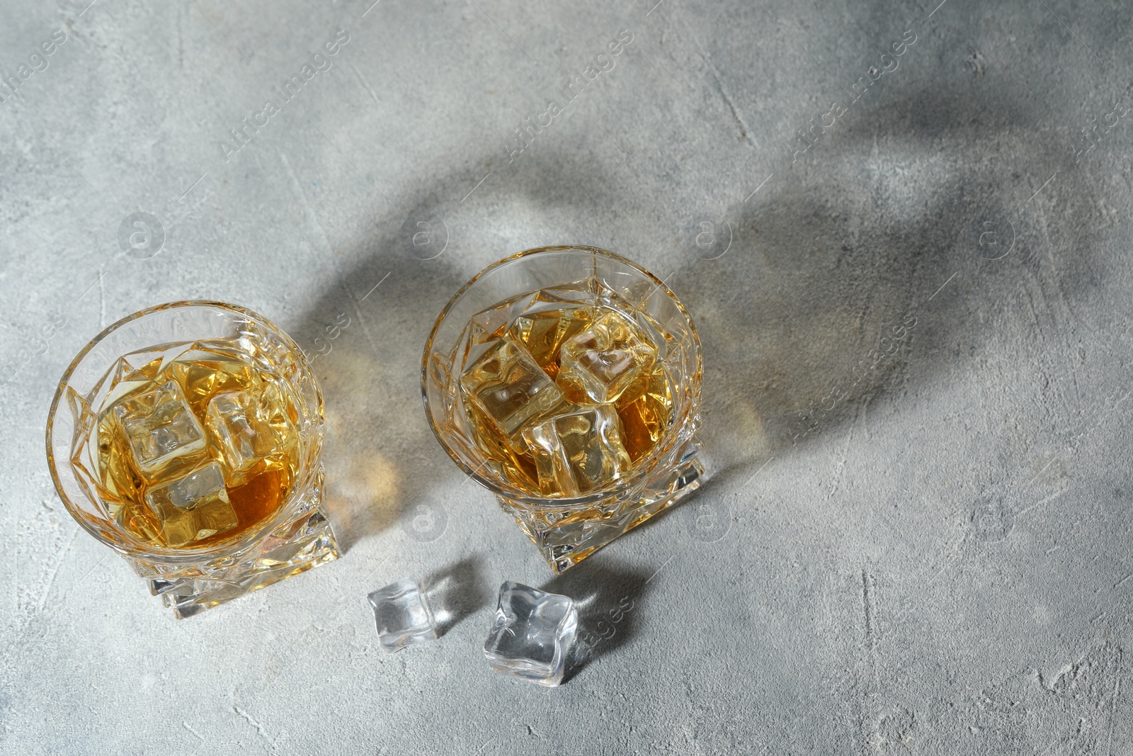 Photo of Whiskey in glasses with ice cubes on grey textured table, above view. Space for text